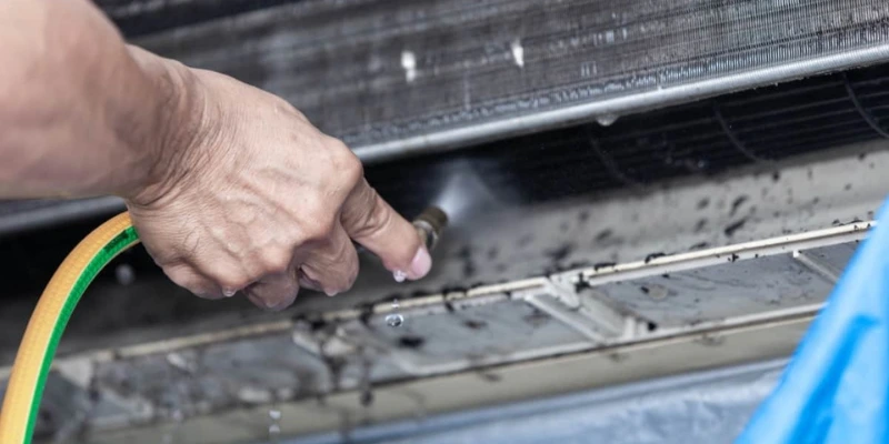 Technician cleaning HVAC evaporator coil with water spray